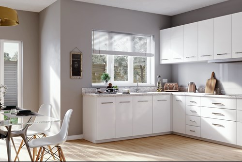 Spacious kitchen with white cupboards and a glass dining table to the left.