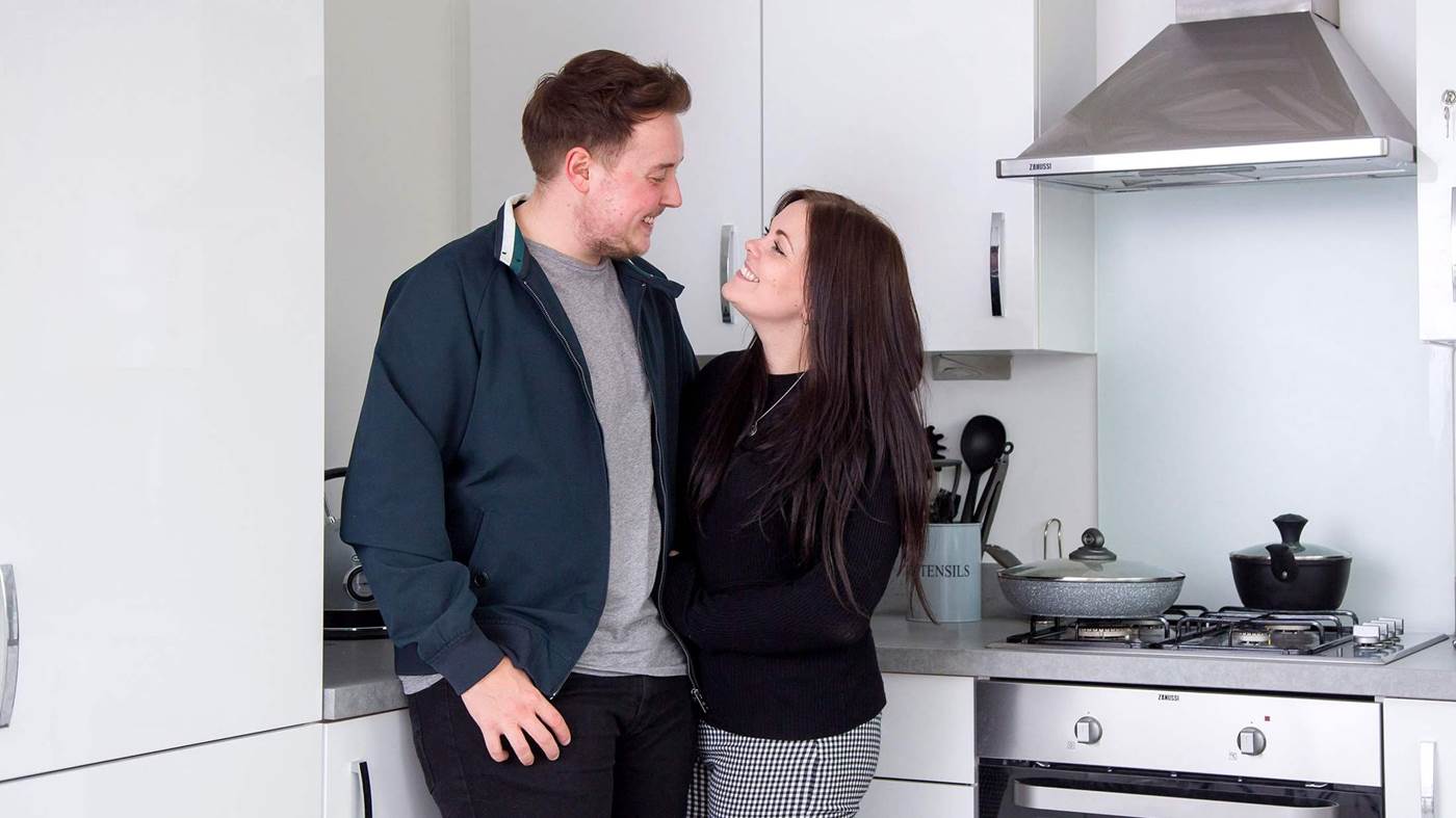 Young couple of first time buyers who bought through shared ownership looking happy in their new kitchen