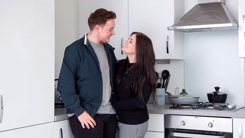 Young couple smiling happily at each other in kitchen space.